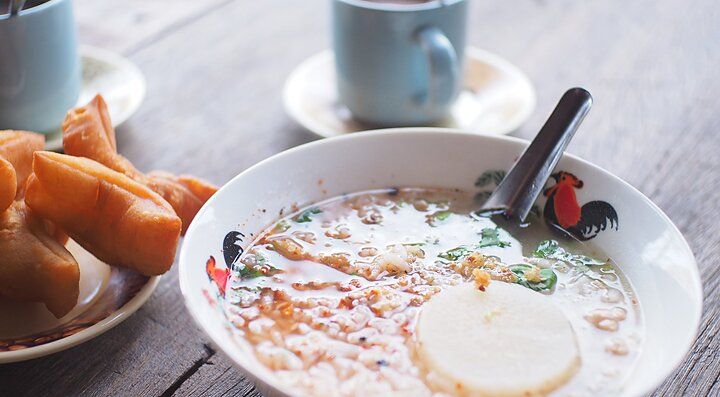 Colazione thailandese con zuppa di riso e pane fritto su tavolo di legno.