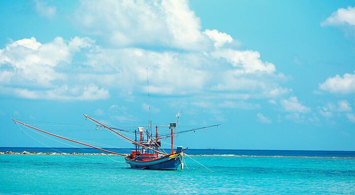Barca tradizionale sul mare turchese di Koh Phangan con cielo nuvoloso.