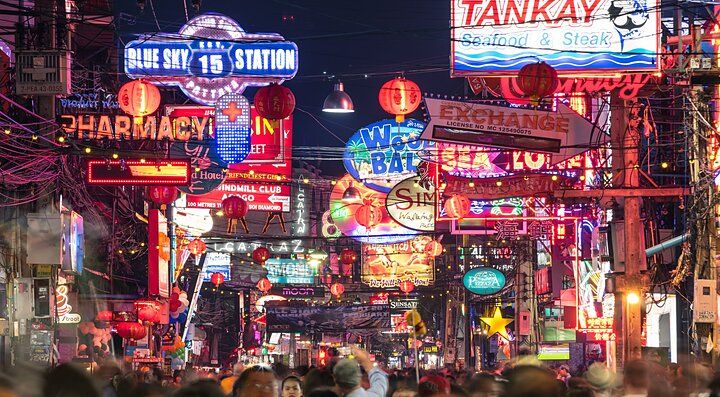 Strada affollata di Pattaya con luci al neon e insegne.
