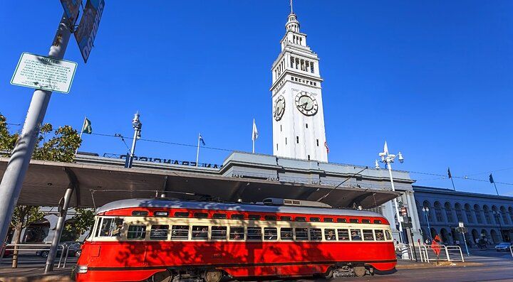 Tram rosso davanti al Ferry Building di San Francisco sotto un cielo blu.