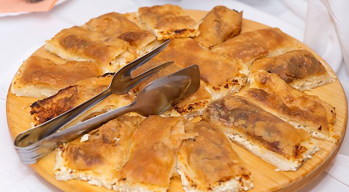 Strudel salato croato servito su un piatto di legno con pinze.