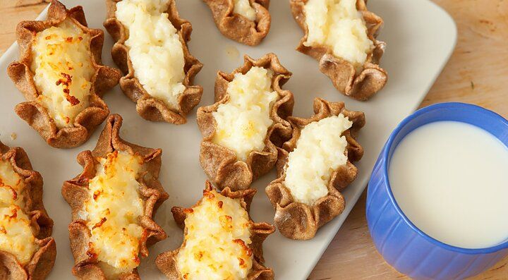 Pasticcini finlandesi con ripieno cremoso su un piatto, accanto a una tazza blu di bevanda bianca.