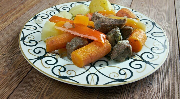 Piatto tradizionale mongolo con carne e verdure colorate su un tavolo di legno.