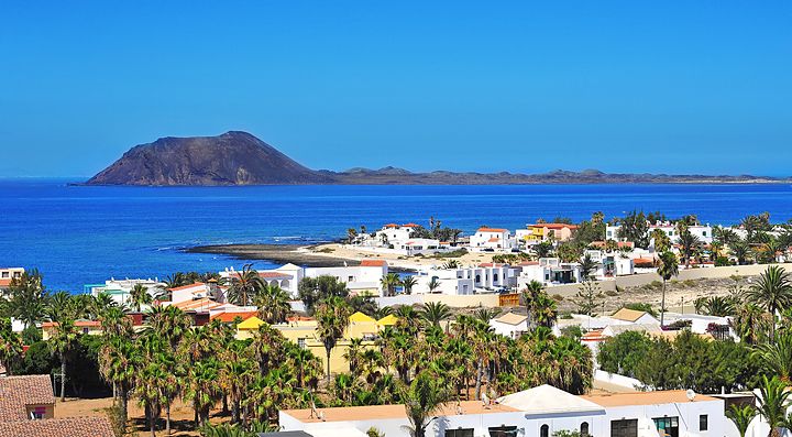 Vista panoramica di un villaggio costiero a Fuerteventura con l'oceano e un'isola sullo sfondo.