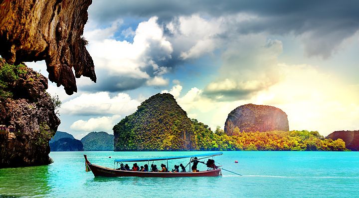 Barca tradizionale naviga nelle acque turchesi di Phuket con isole sullo sfondo.