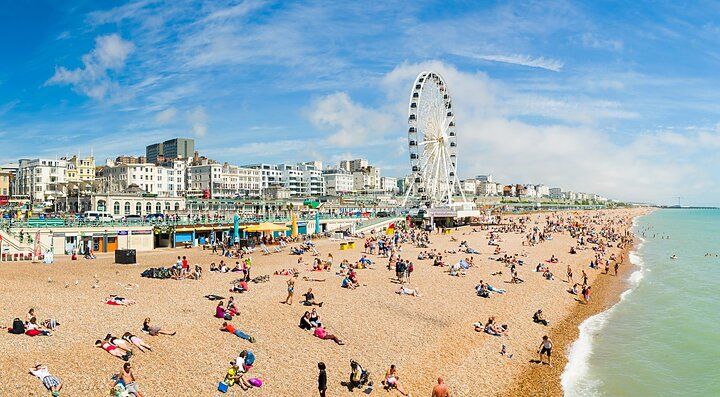 Spiaggia affollata di Brighton con ruota panoramica e edifici sullo sfondo.