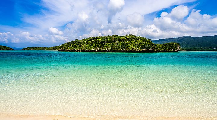 La spiaggia di Ishigaki con acque cristalline e un'isola verde all'orizzonte.