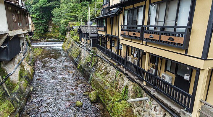 Edifici tradizionali lungo un fiume a Kurokawa Onsen, immersi nella natura.