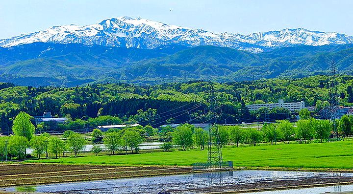 Paesaggio del Monte Hakusan con neve sulle cime e campagna verde in primo piano.