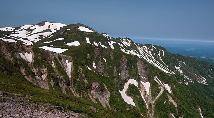 Veduta del Monte Kurodake con neve sulle cime e verde lungo i pendii.