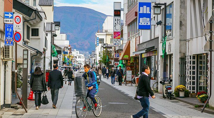 Strada commerciale a Nakamachi, con persone che camminano e vanno in bici.