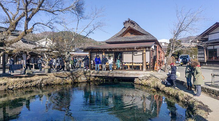 Lago di Oshino Hakkai con persone che ammirano l'acqua e le costruzioni tradizionali circostanti.