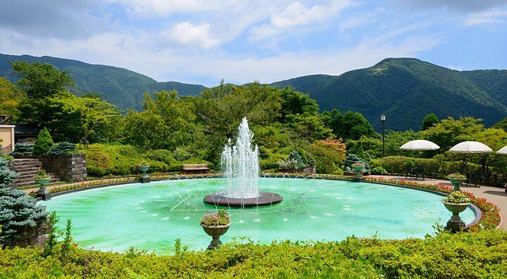 Fontana circondata da verde al Parco Gora, con montagne sullo sfondo.