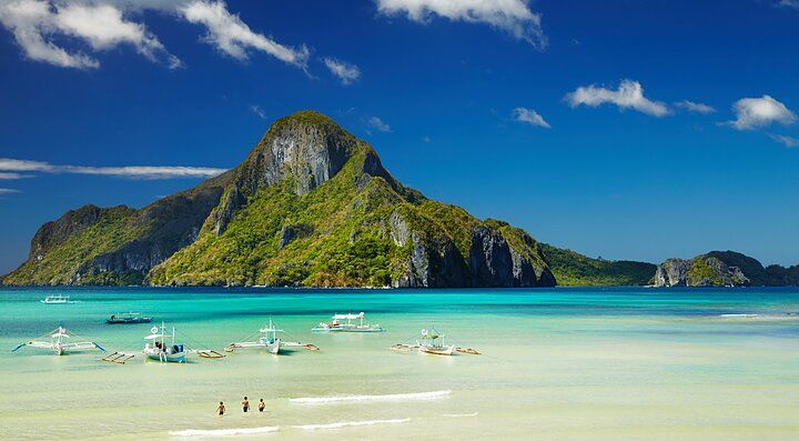 Spiaggia tropicale delle Filippine con montagne e barche sull'acqua.