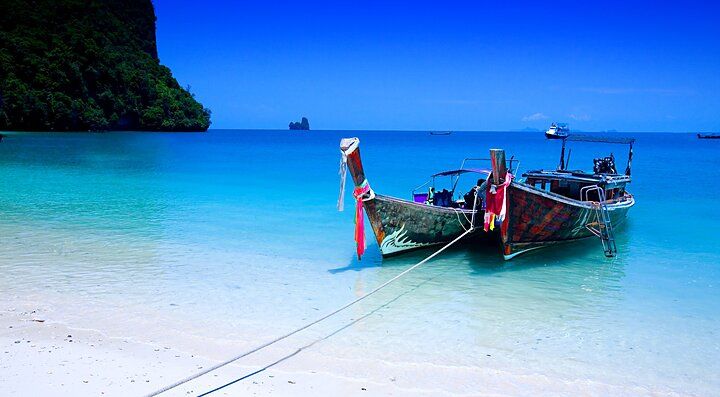 Barca tradizionale sulla spiaggia di Krabi, mare cristallino e cielo blu.