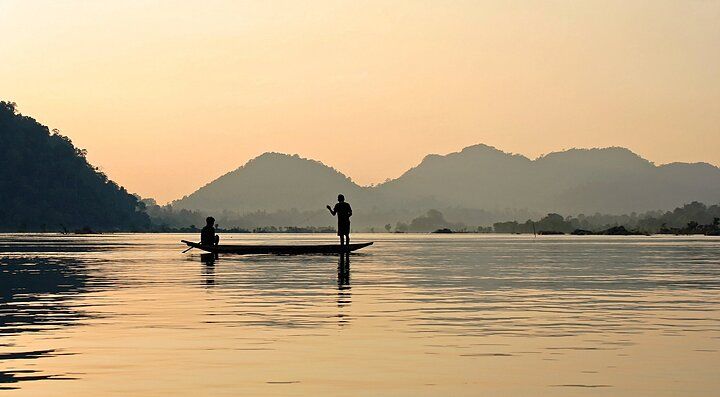 Pescatori su una barca al tramonto in un fiume in Laos.
