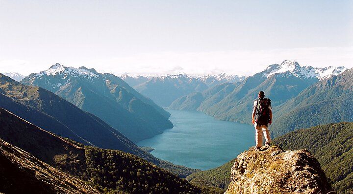 Escursionista su un promontorio con vista su montagne e lago in Nuova Zelanda.