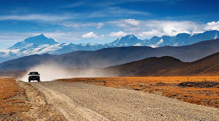 Auto su strada sterrata con montagne del Tibet sullo sfondo.