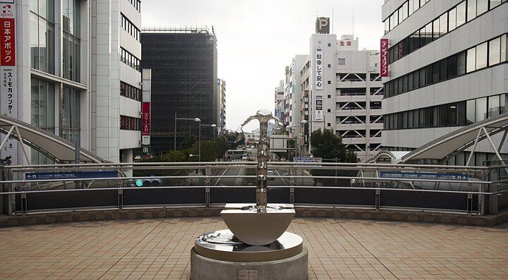 Vista urbana di Saitama con edifici moderni e una fontana in primo piano.