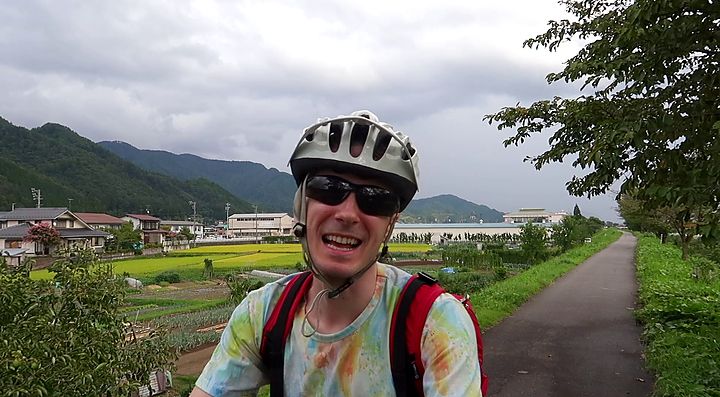 Ciclista su un sentiero rurale a Satoyama circondato da campi e montagne.