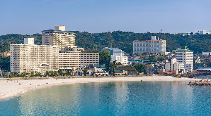 Spiaggia di Shirahama con edifici sulla riva e colline verdi sullo sfondo.