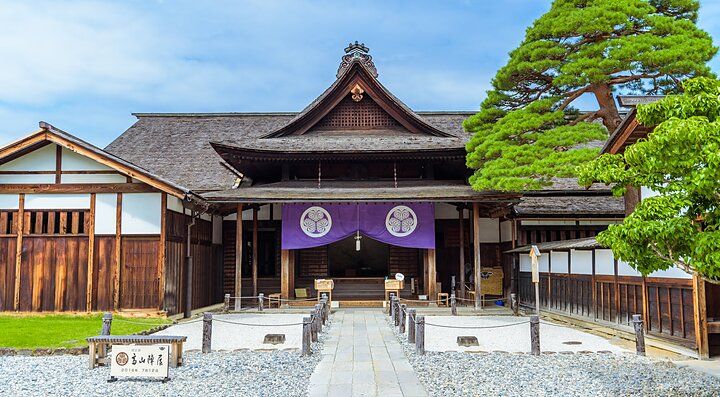 Takayama Jinya, edificio storico in legno con giardino pietroso e albero verde.