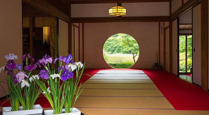 Interno del tempio Meigetsuin con tatami e fiori davanti a una finestra circolare.