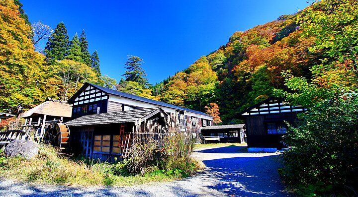 Edifici tradizionali circondati da colline boscose a Tsurunoyu Onsen in autunno.