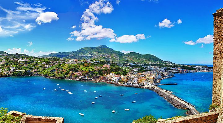Veduta panoramica di Ischia con il mare blu e il paesaggio collinare.