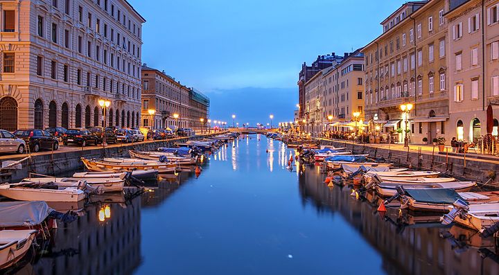 Canal Grande a Trieste al tramonto con barche e palazzi illuminati.
