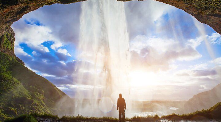 Una persona ammira una cascata in Islanda con il cielo nuvoloso.
