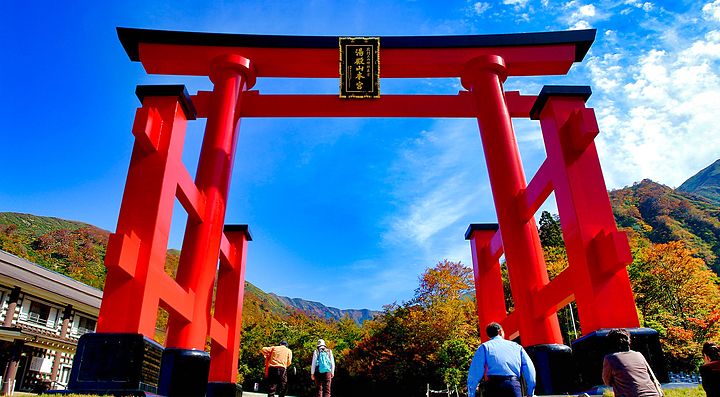 Grande torii rosso a Yudono-san, incorniciato da alberi e montagne.