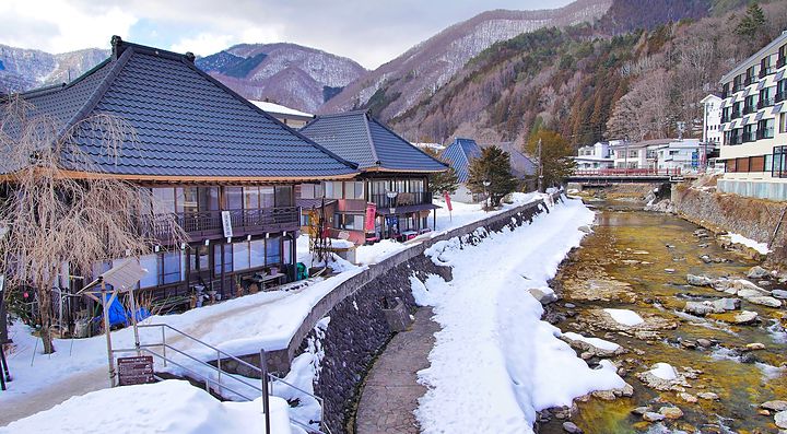 Il paesaggio invernale di Yunishigawa Onsen con fiume e montagne innevate.