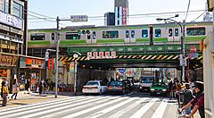 Treno sopra un ponte a Shin-Ōkubo, Tokyo, con traffico e pedoni.