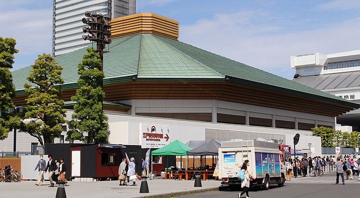 Il Ryogoku Kokugikan a Tokyo con visitatori e camion nel parcheggio.