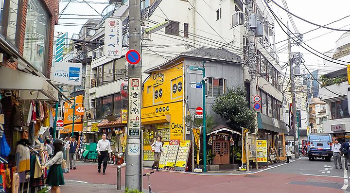 Strada commerciale nel quartiere Shimokitazawa, Tokyo, con negozi e passanti.