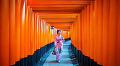 Donna in kimono cammina tra i torii arancioni di Fushimi Inari a Kyoto.