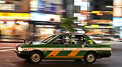 Taxi verde e giallo in movimento per le strade illuminate di Tokyo.