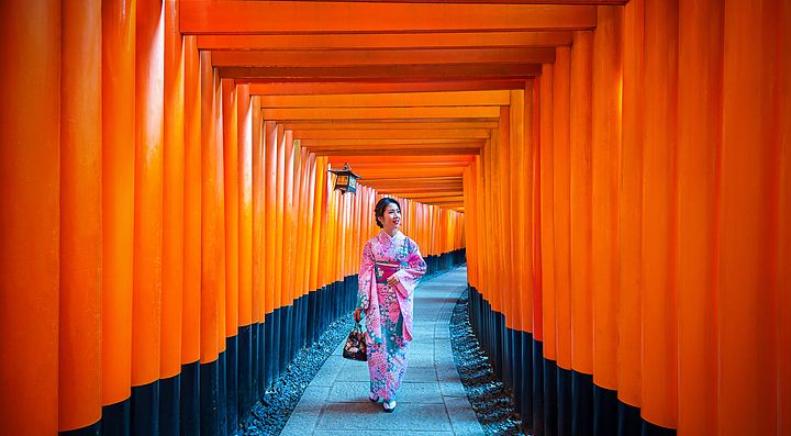 Donna in kimono cammina tra i torii arancioni di Fushimi Inari a Kyoto.