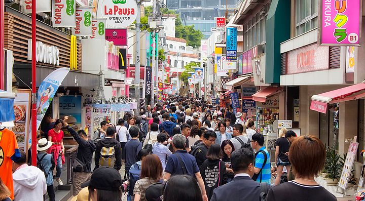 Strada affollata a Harajuku con negozi colorati e passanti.
