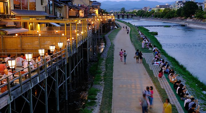 Persone camminano al tramonto sulle rive del fiume Kamogawa a Kyoto.