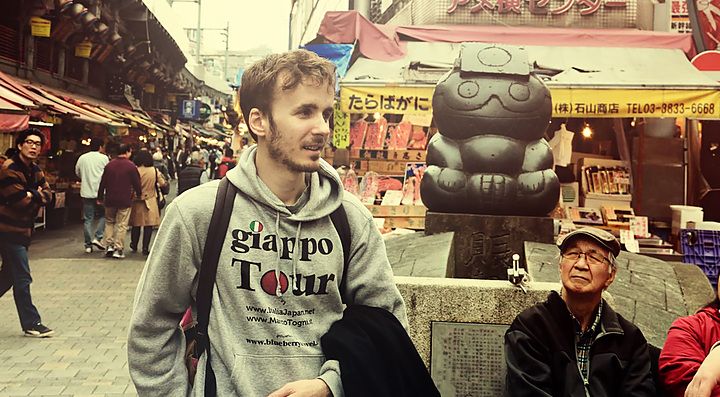 Marco Togni a Ueno, Tokyo, in un mercato affollato con una statua sullo sfondo.