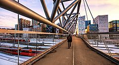 Ponte pedonale moderno a Oslo con edifici e treni sullo sfondo.
