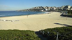 Spiaggia di Coogee con sabbia dorata e mare calmo, edifici in lontananza.