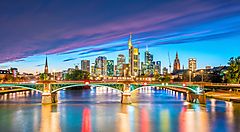 Skyline di Francoforte al tramonto con un ponte illuminato sul fiume.