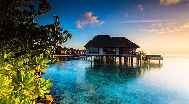 Bungalow su palafitte alle Maldive al tramonto.