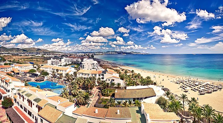 Spiaggia e edifici lungo la costa di Ibiza sotto un cielo azzurro.