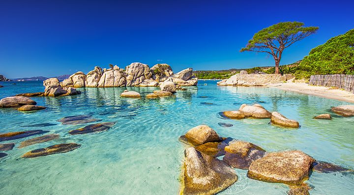 Spiaggia rocciosa e mare cristallino in Corsica sotto un cielo blu.