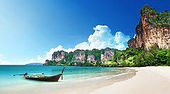 Spiaggia thailandese con barca tradizionale e scogliere sullo sfondo.