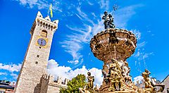 Fontana del Nettuno e Torre Civica a Trento sotto un cielo azzurro.